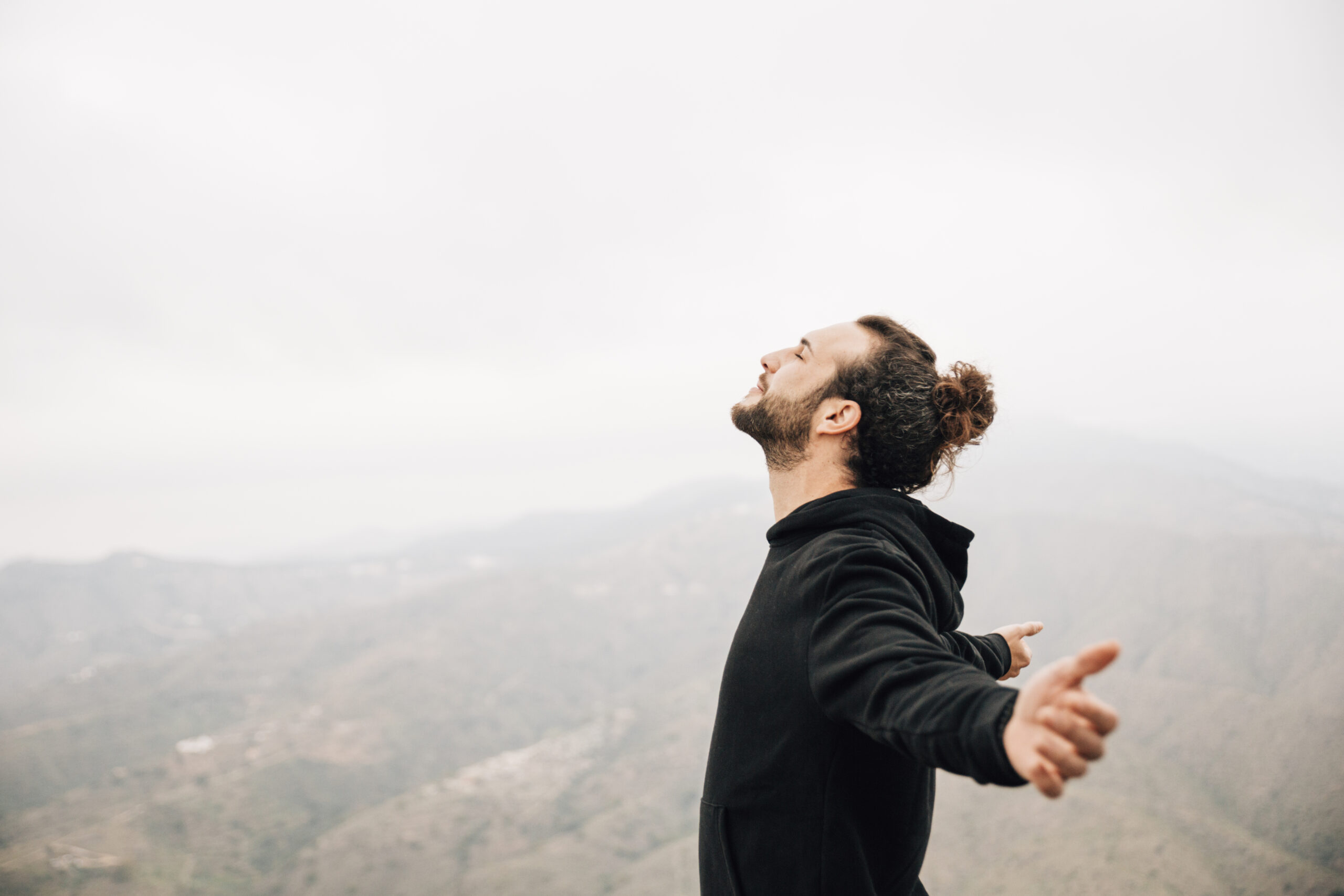 Hombre de perfil frente a las montañas con los brazos abiertos