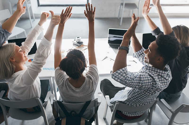 Equipo de trabajo celebrando con los brazos en alto alrededor de una mesa