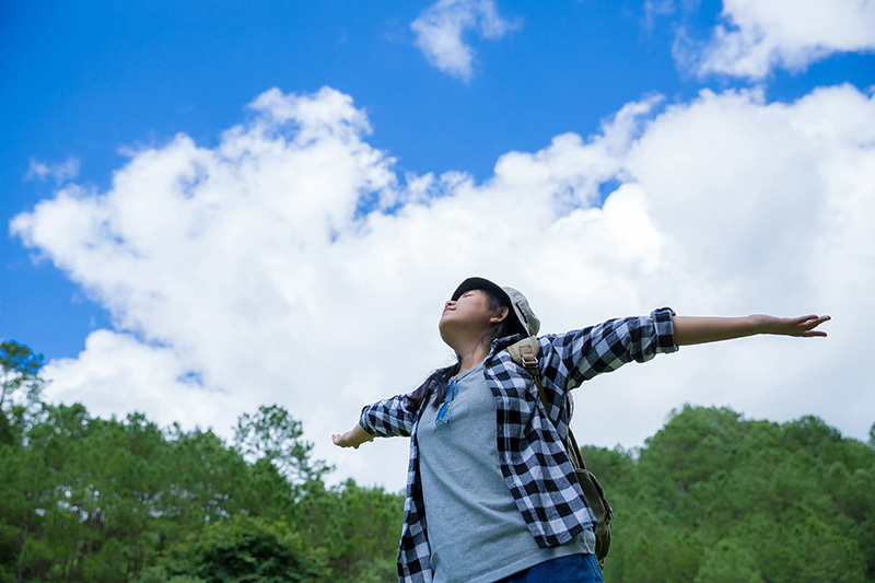 Persona con los brazos abiertos bajo un cielo con nubes